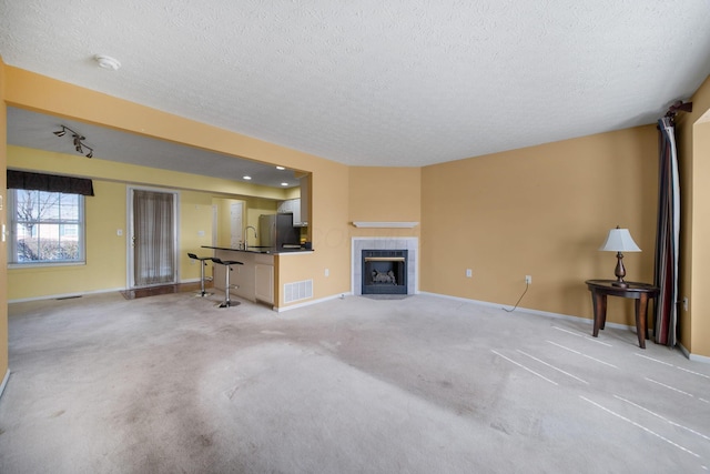 unfurnished living room featuring visible vents, baseboards, light carpet, a tile fireplace, and a textured ceiling