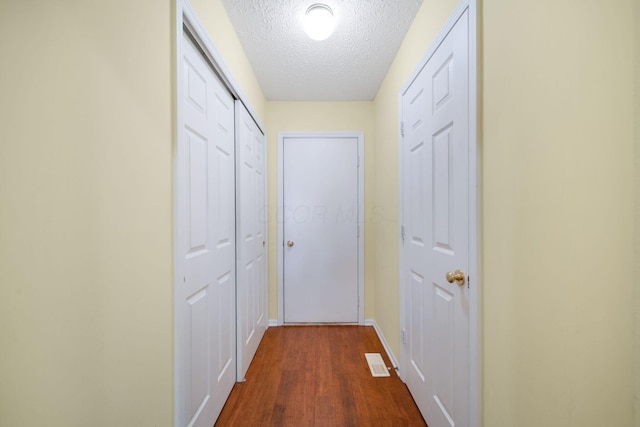 corridor featuring dark wood-type flooring, baseboards, visible vents, and a textured ceiling