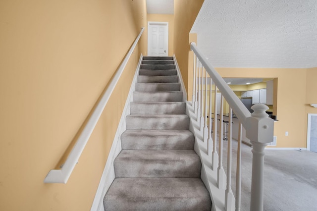 stairs featuring a textured ceiling, baseboards, and carpet floors