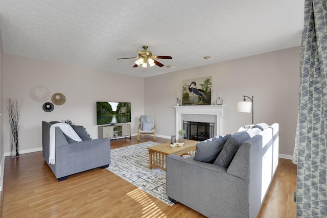 living area featuring a textured ceiling, wood finished floors, a fireplace, baseboards, and ceiling fan