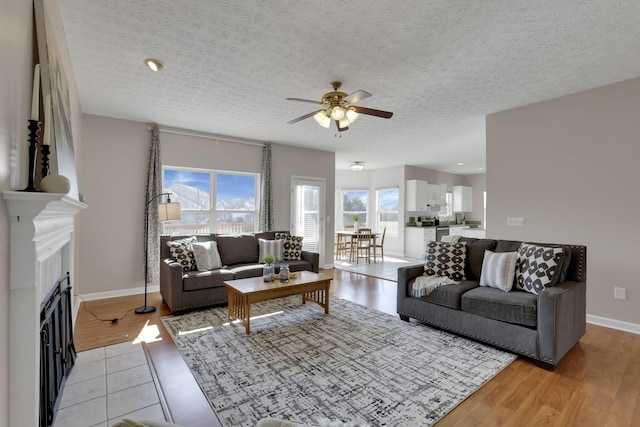 living room featuring a ceiling fan, a fireplace, light wood finished floors, and a textured ceiling