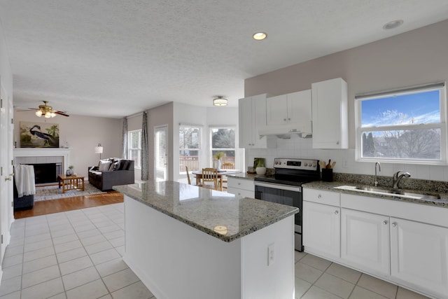 kitchen with light tile patterned floors, electric range, a tile fireplace, a sink, and a center island