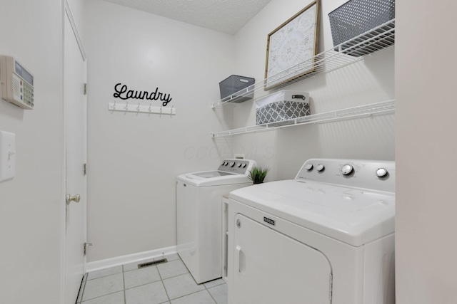 clothes washing area with visible vents, a textured ceiling, separate washer and dryer, light tile patterned flooring, and laundry area