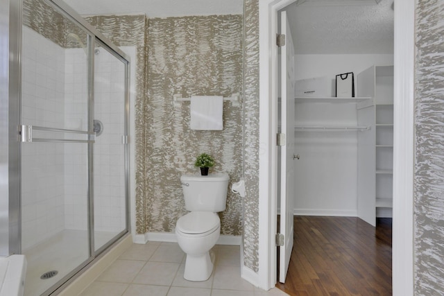 full bathroom with wallpapered walls, baseboards, toilet, a stall shower, and a textured ceiling