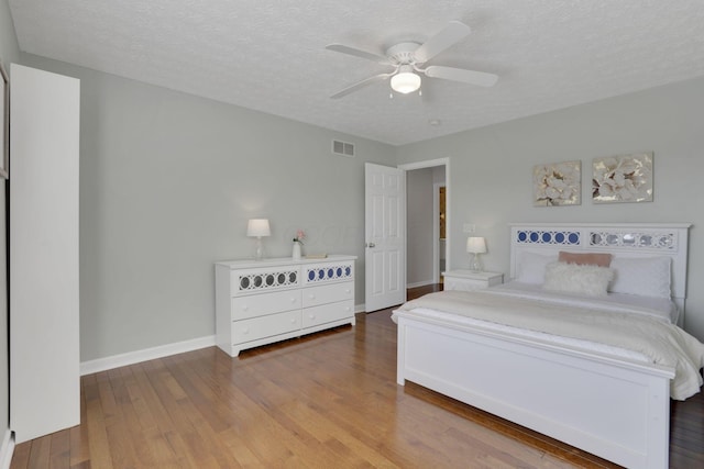 bedroom featuring visible vents, a ceiling fan, a textured ceiling, wood finished floors, and baseboards