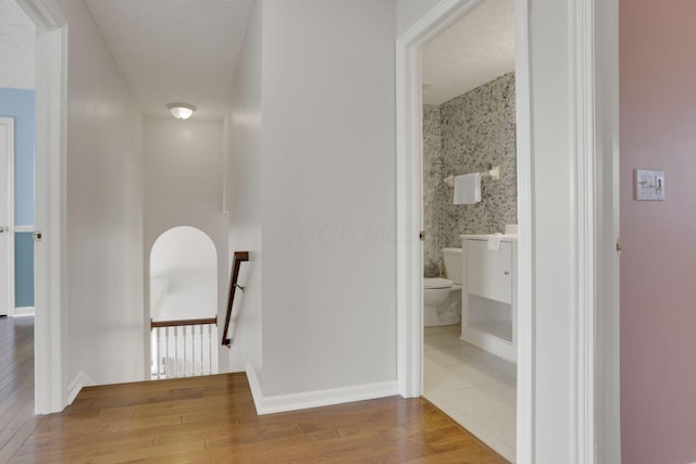 corridor with an upstairs landing, baseboards, wood finished floors, and wallpapered walls