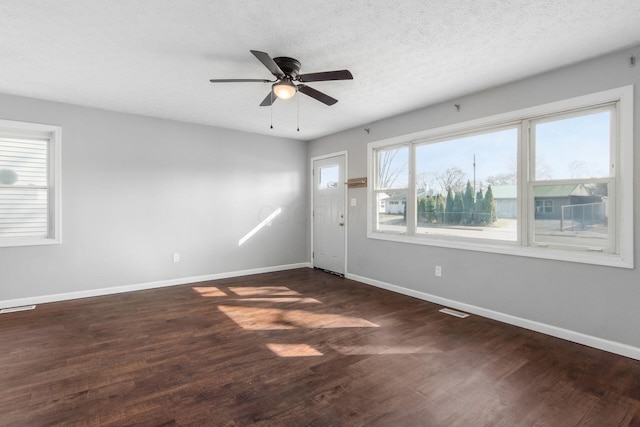 unfurnished room with dark wood-type flooring, visible vents, baseboards, and a textured ceiling