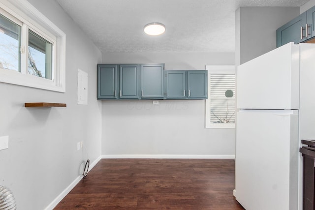 kitchen with blue cabinets, dark wood-style floors, baseboards, and freestanding refrigerator