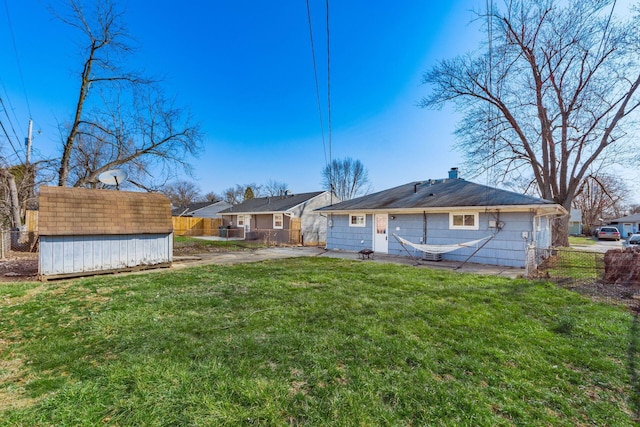 rear view of property featuring a shed, an outdoor structure, a yard, and fence