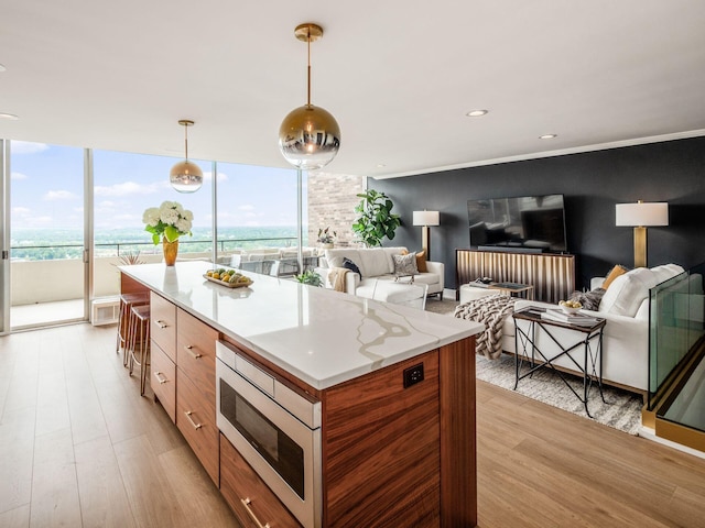 kitchen featuring modern cabinets, decorative light fixtures, stainless steel microwave, a center island, and light wood finished floors