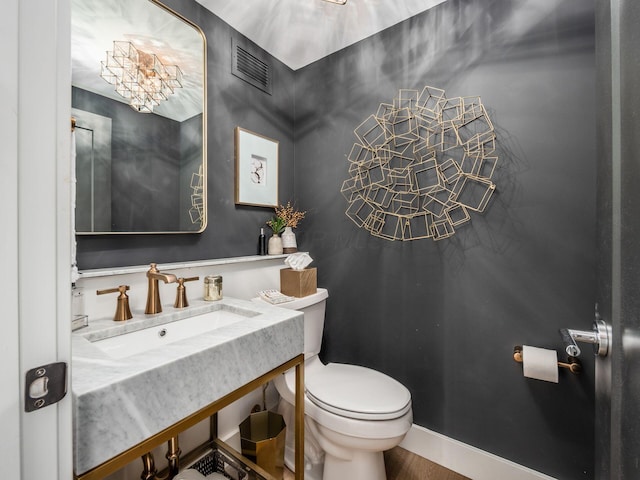 half bath featuring vanity, toilet, baseboards, and visible vents