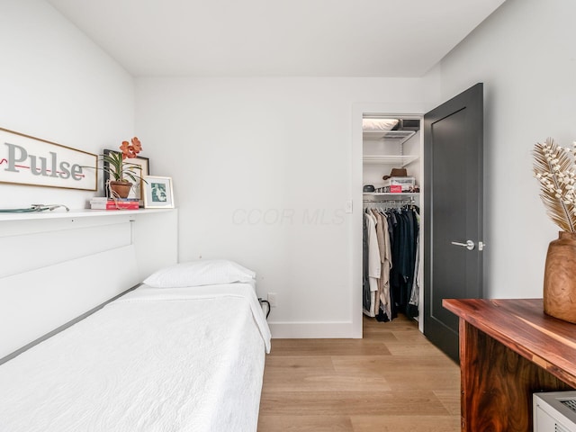 bedroom with a closet, baseboards, a walk in closet, and light wood-style flooring