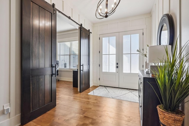 entryway featuring a barn door, a notable chandelier, baseboards, and light wood finished floors