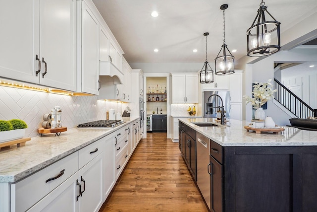 kitchen with light wood-type flooring, an island with sink, a sink, appliances with stainless steel finishes, and white cabinets