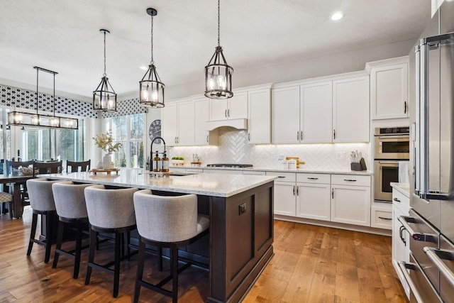 kitchen with a breakfast bar area, appliances with stainless steel finishes, white cabinets, and hardwood / wood-style flooring