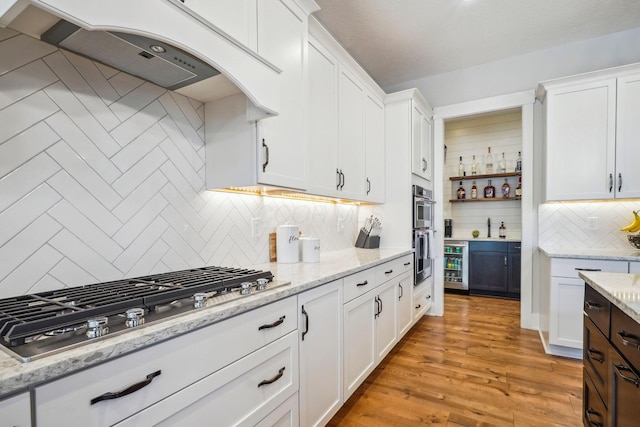 kitchen featuring ventilation hood, stainless steel appliances, light wood-type flooring, and white cabinets