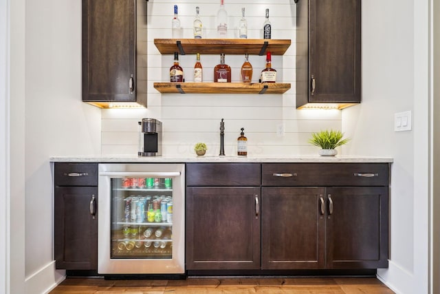 bar with wood finished floors, wine cooler, a bar, decorative backsplash, and baseboards