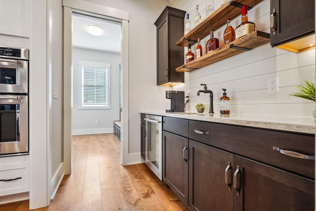 kitchen featuring light wood-type flooring, stainless steel double oven, wine cooler, baseboards, and dark brown cabinets