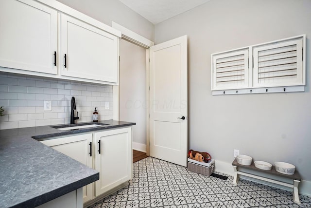 interior space featuring white cabinetry, dark countertops, backsplash, and a sink