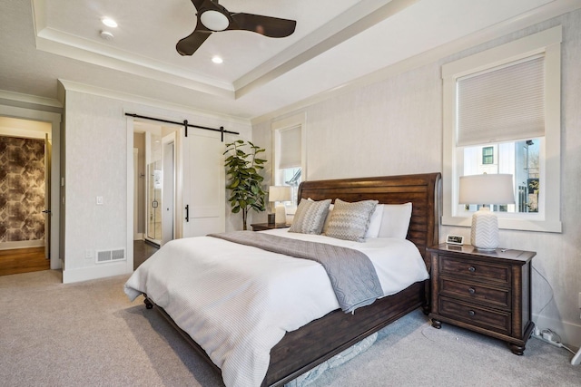 carpeted bedroom with a tray ceiling, multiple windows, and a barn door