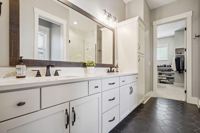 full bath with double vanity, a sink, a shower stall, a walk in closet, and tile patterned floors