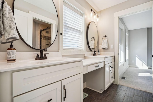 full bath with visible vents, a sink, wood finished floors, a shower stall, and double vanity