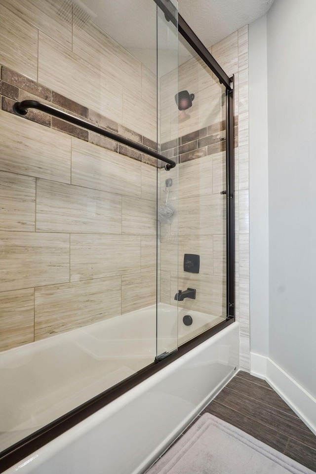 bathroom featuring enclosed tub / shower combo, baseboards, and wood finished floors