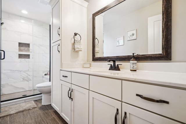 bathroom with a shower stall, toilet, vanity, and wood finish floors