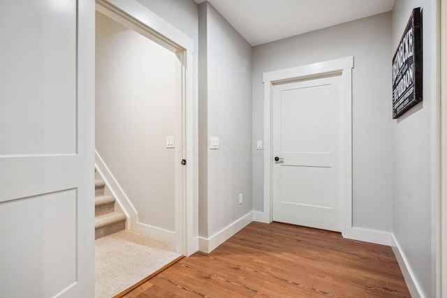 hallway with light wood-type flooring, baseboards, and stairs