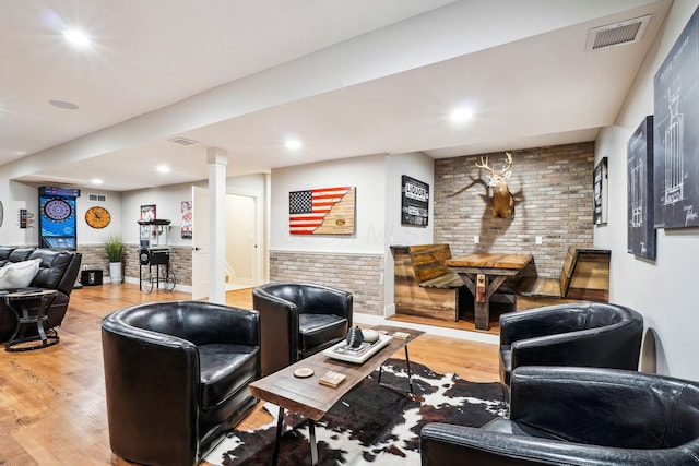 living area with recessed lighting, visible vents, wood finished floors, and brick wall