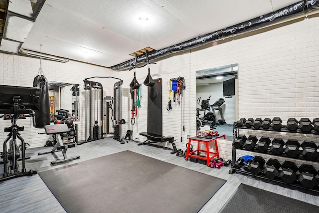 exercise area featuring brick wall and wood finished floors