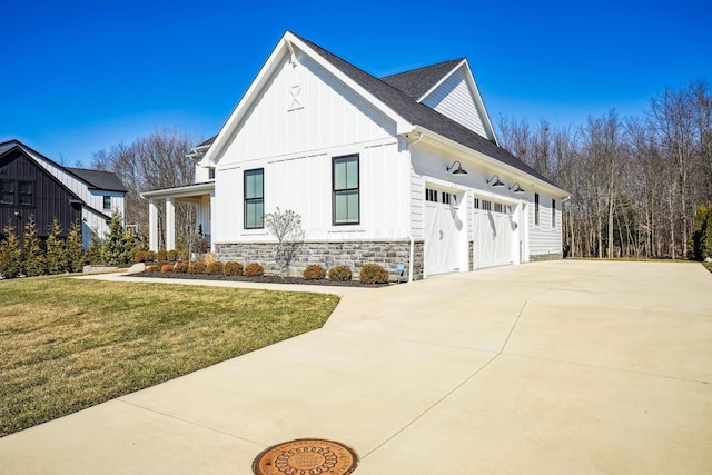 view of home's exterior featuring driveway, stone siding, a yard, board and batten siding, and a garage