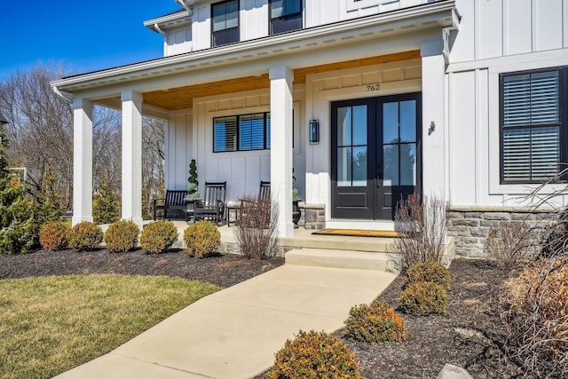 view of exterior entry featuring a porch, french doors, board and batten siding, and stone siding