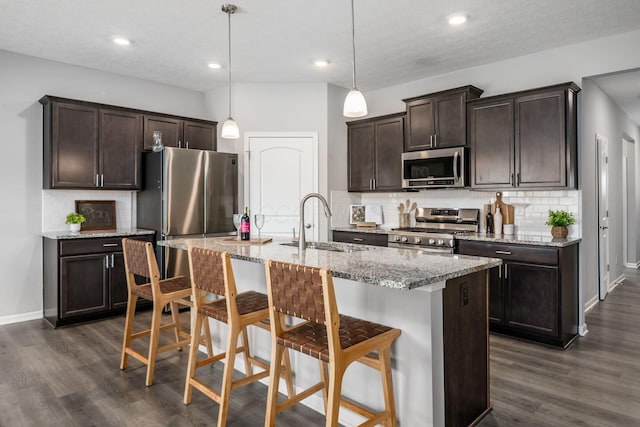 kitchen featuring dark brown cabinetry, dark wood finished floors, a breakfast bar, appliances with stainless steel finishes, and a sink