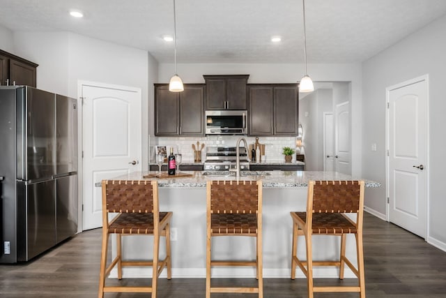 kitchen with tasteful backsplash, light stone countertops, dark brown cabinetry, dark wood finished floors, and appliances with stainless steel finishes