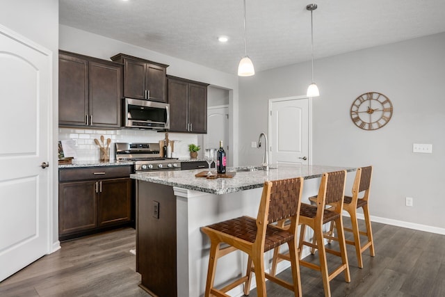 kitchen with a breakfast bar, light stone counters, decorative backsplash, appliances with stainless steel finishes, and dark wood-style floors