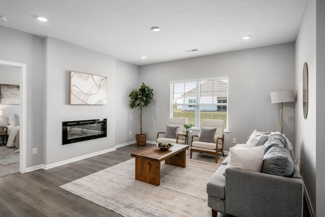 living area with a glass covered fireplace, recessed lighting, wood finished floors, and baseboards