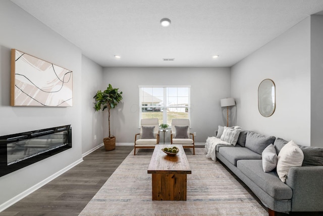 living area with visible vents, baseboards, recessed lighting, wood finished floors, and a glass covered fireplace