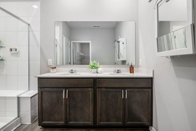 full bathroom featuring a sink, visible vents, tiled shower, and double vanity