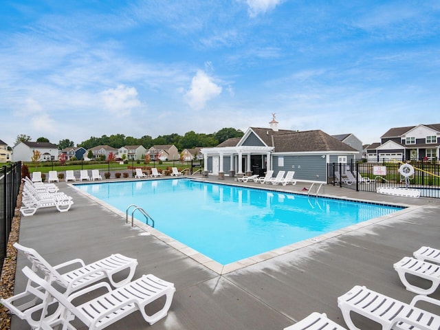 community pool featuring a patio area, a residential view, an outbuilding, and fence