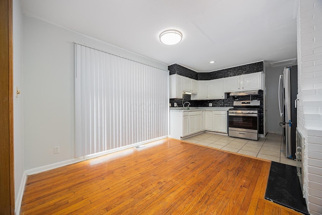 kitchen featuring a sink, stainless steel appliances, white cabinets, under cabinet range hood, and backsplash