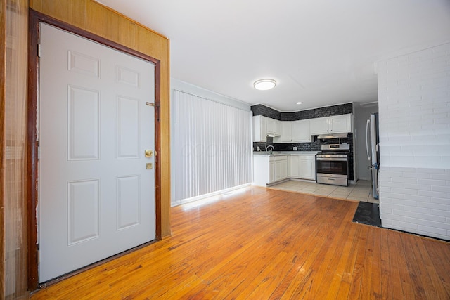 kitchen featuring appliances with stainless steel finishes, white cabinets, light wood finished floors, decorative backsplash, and light countertops