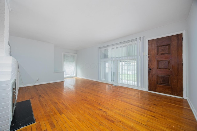 unfurnished living room featuring visible vents, baseboards, a brick fireplace, and hardwood / wood-style floors