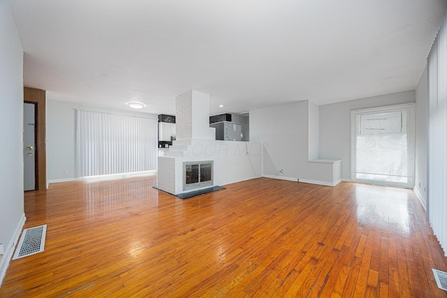 unfurnished living room with hardwood / wood-style floors, a fireplace, visible vents, and baseboards