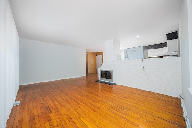 unfurnished living room featuring visible vents, a fireplace with raised hearth, baseboards, and hardwood / wood-style floors