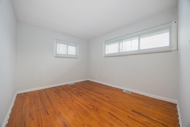 spare room with visible vents, baseboards, and wood finished floors