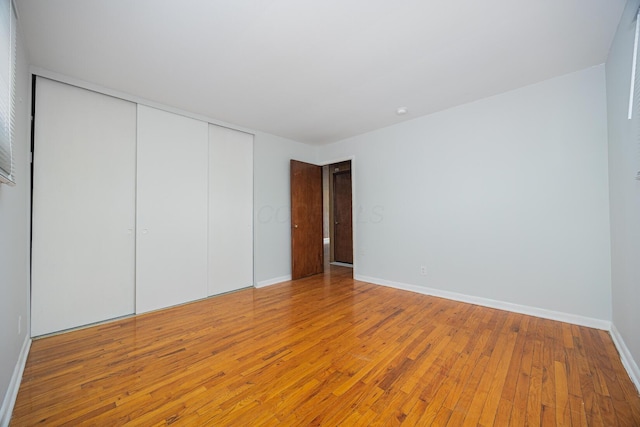 unfurnished bedroom featuring hardwood / wood-style floors, baseboards, and a closet