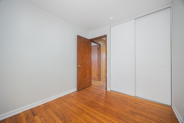 unfurnished bedroom with wood finished floors, baseboards, and a closet