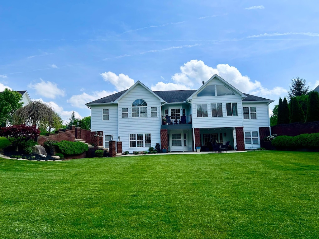 back of property with a lawn, brick siding, and a patio area