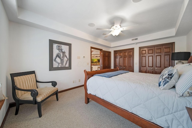 bedroom featuring baseboards, visible vents, multiple closets, a raised ceiling, and carpet flooring